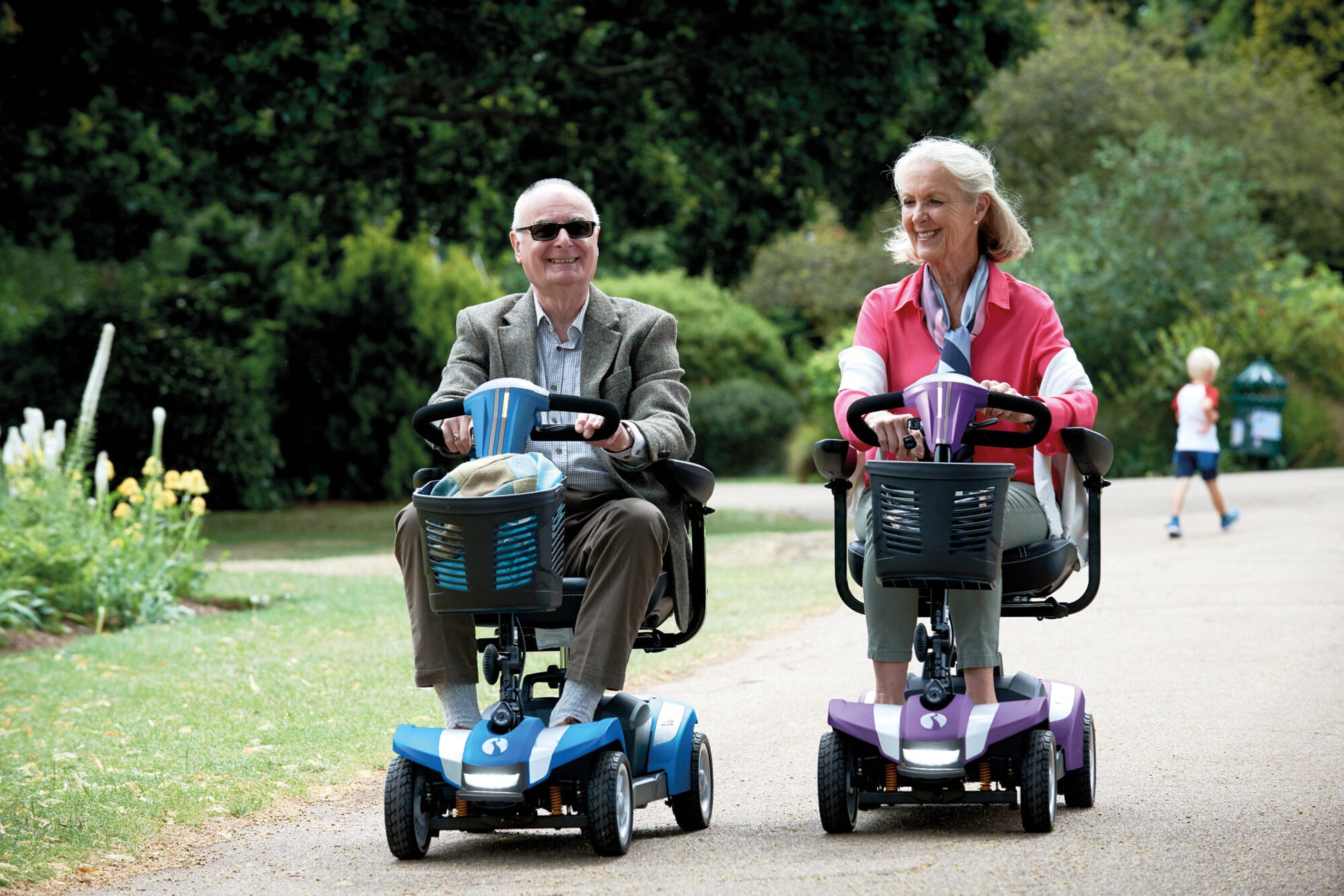 Showing Veo Sport in the colour blue being driven by a man and The veo sport in the colour purple being driven by a woman side by side in the park.