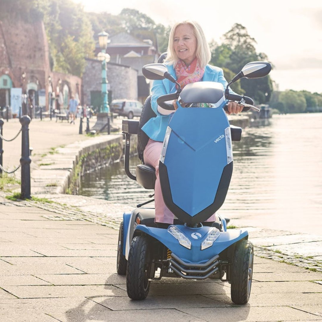 Showing the Rascal Vecta Sport being driven by a lady on a summers day near a river. She looks happy and stylish on her new scooter